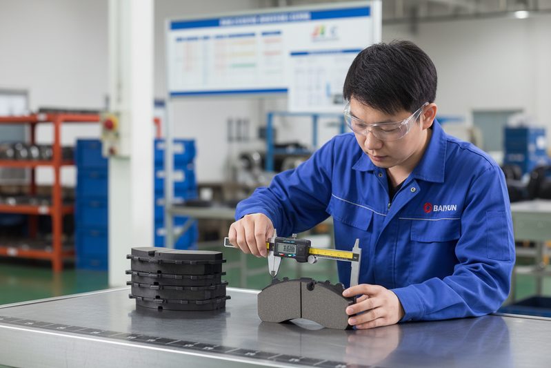 白云制动/刹车片工厂技术员在通过IATF 16949认证的设施中，在生产线上检查一批静音陶瓷刹车片。